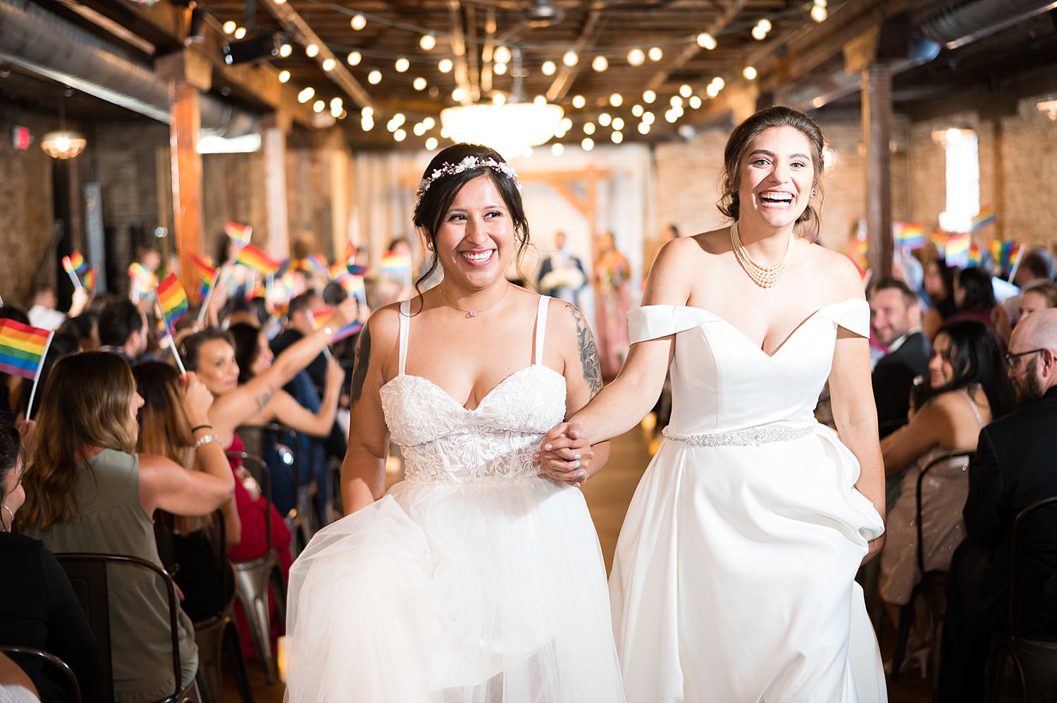 Guest wave rainbow flags as brides walk down wedding aisle at The Haight.
