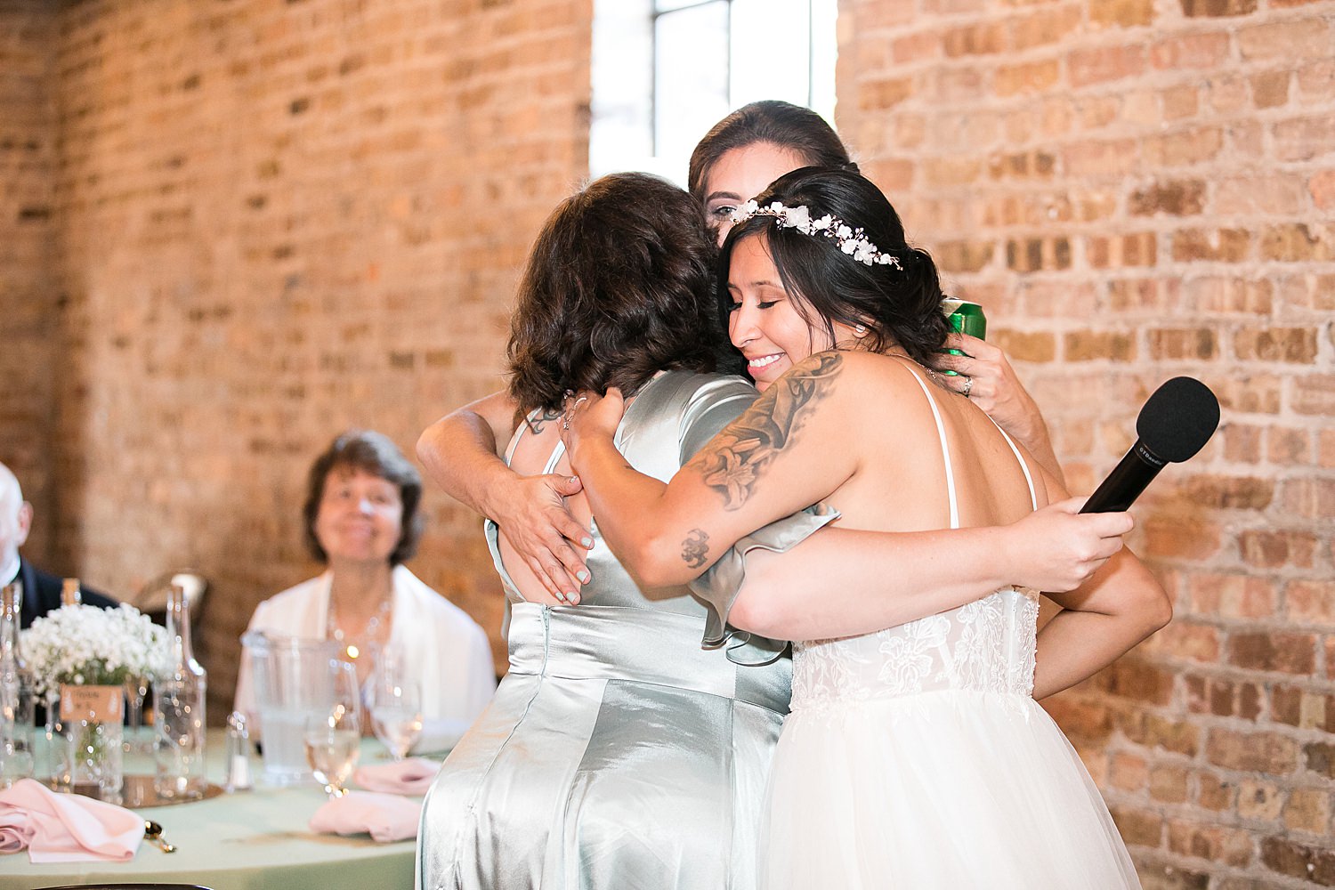 Brides hug maid of honor at wedding reception.