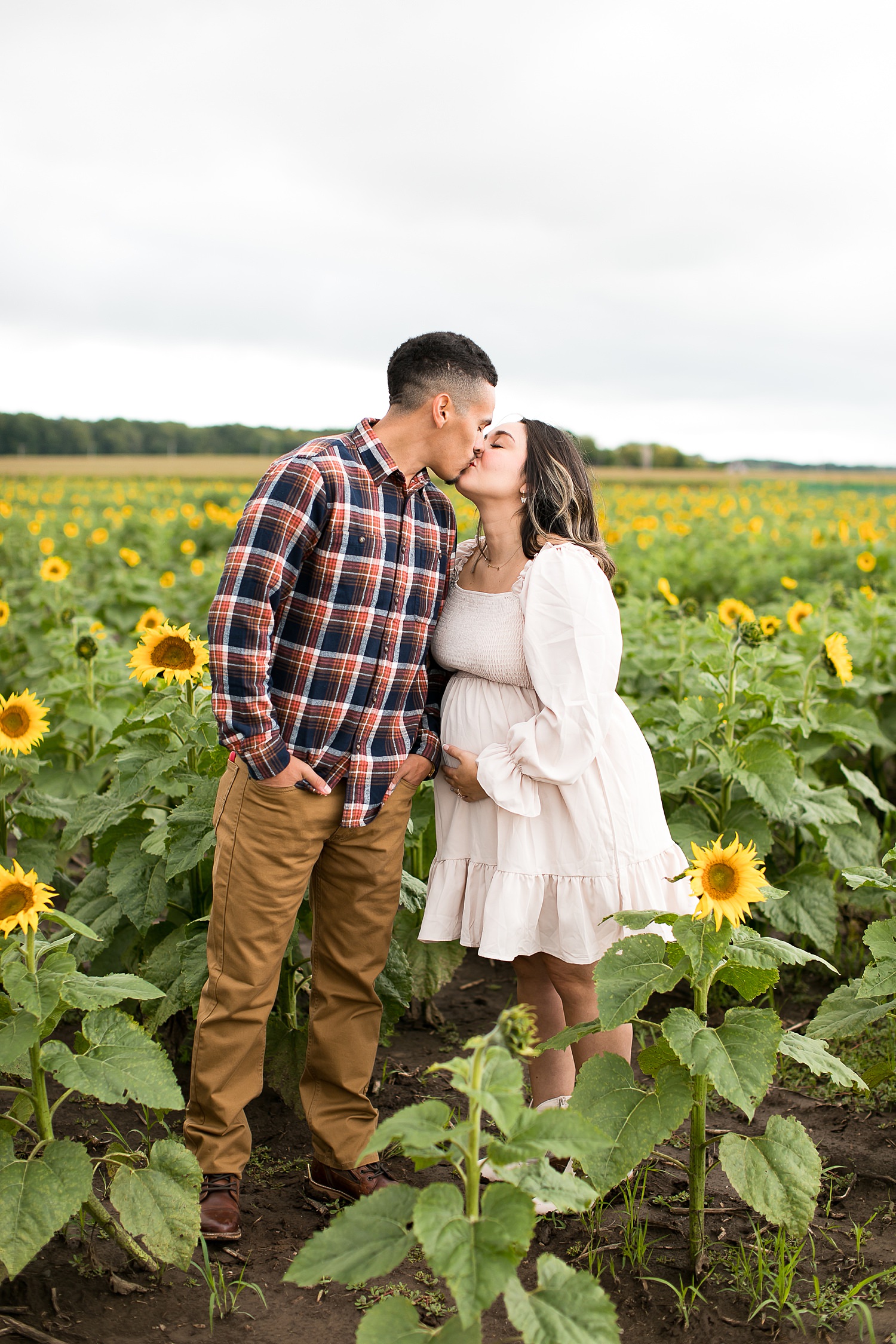 Couple stands in sunflower field for maternity photos