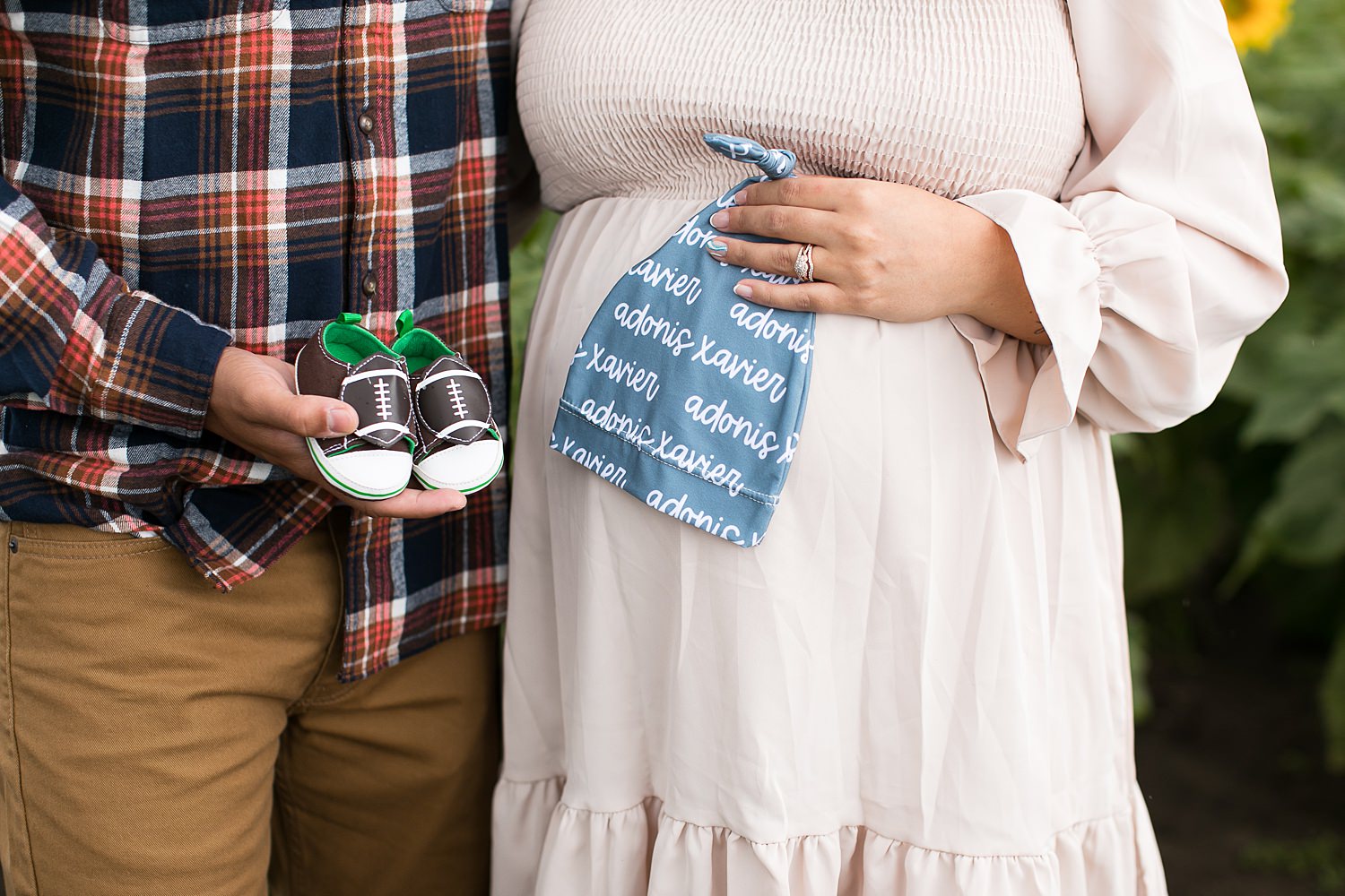 Couples holds baby shoes and hat for maternity photo session