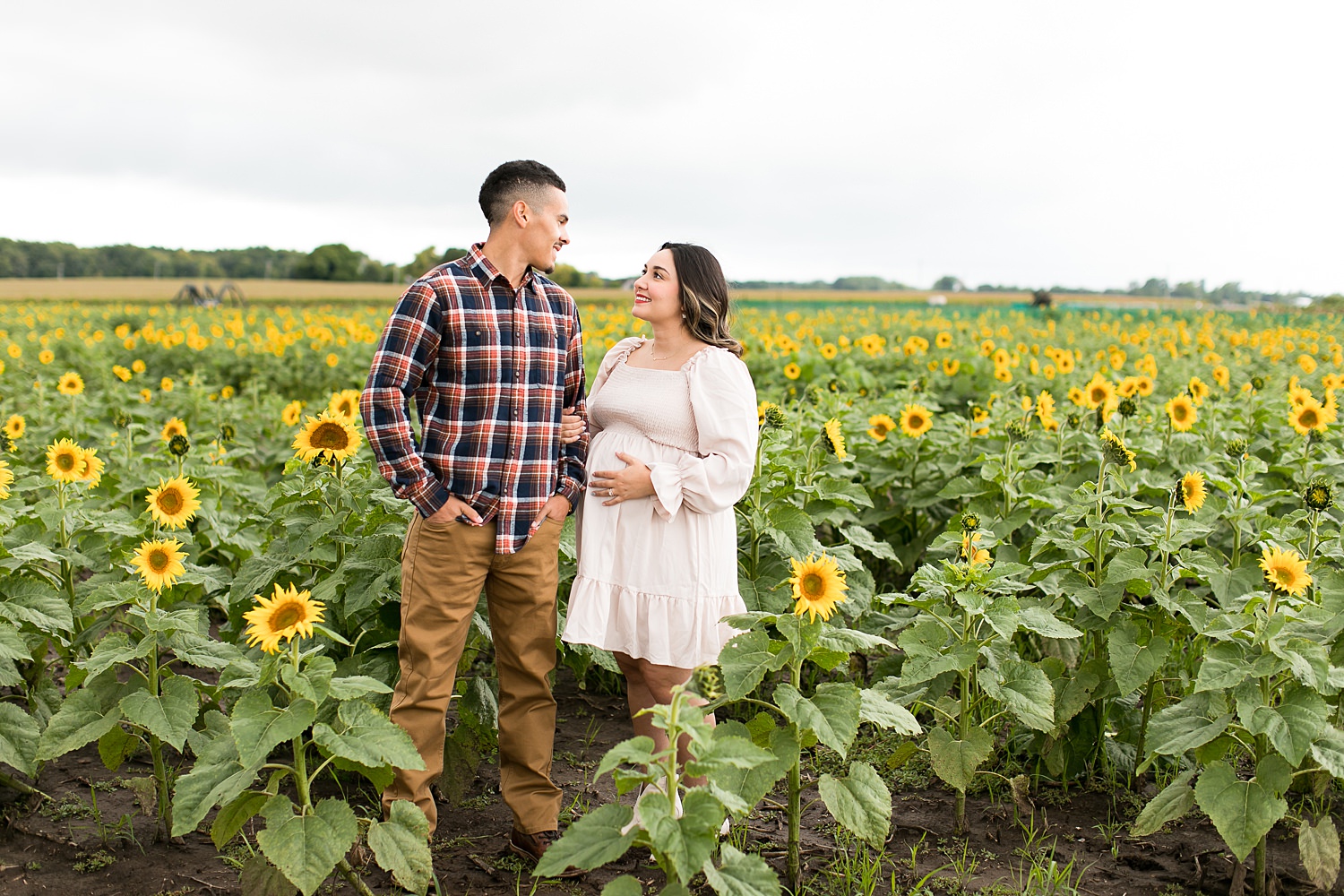 Couple holds hand in sunflower field for maternity photos